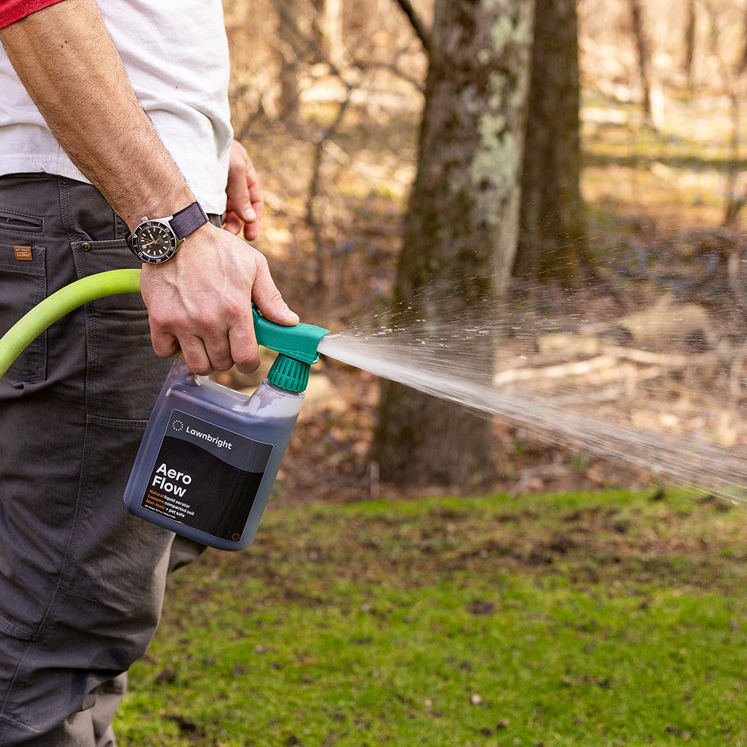Person using a spray bottle labeled 'Aeroflow' with a garden hose outdoors.