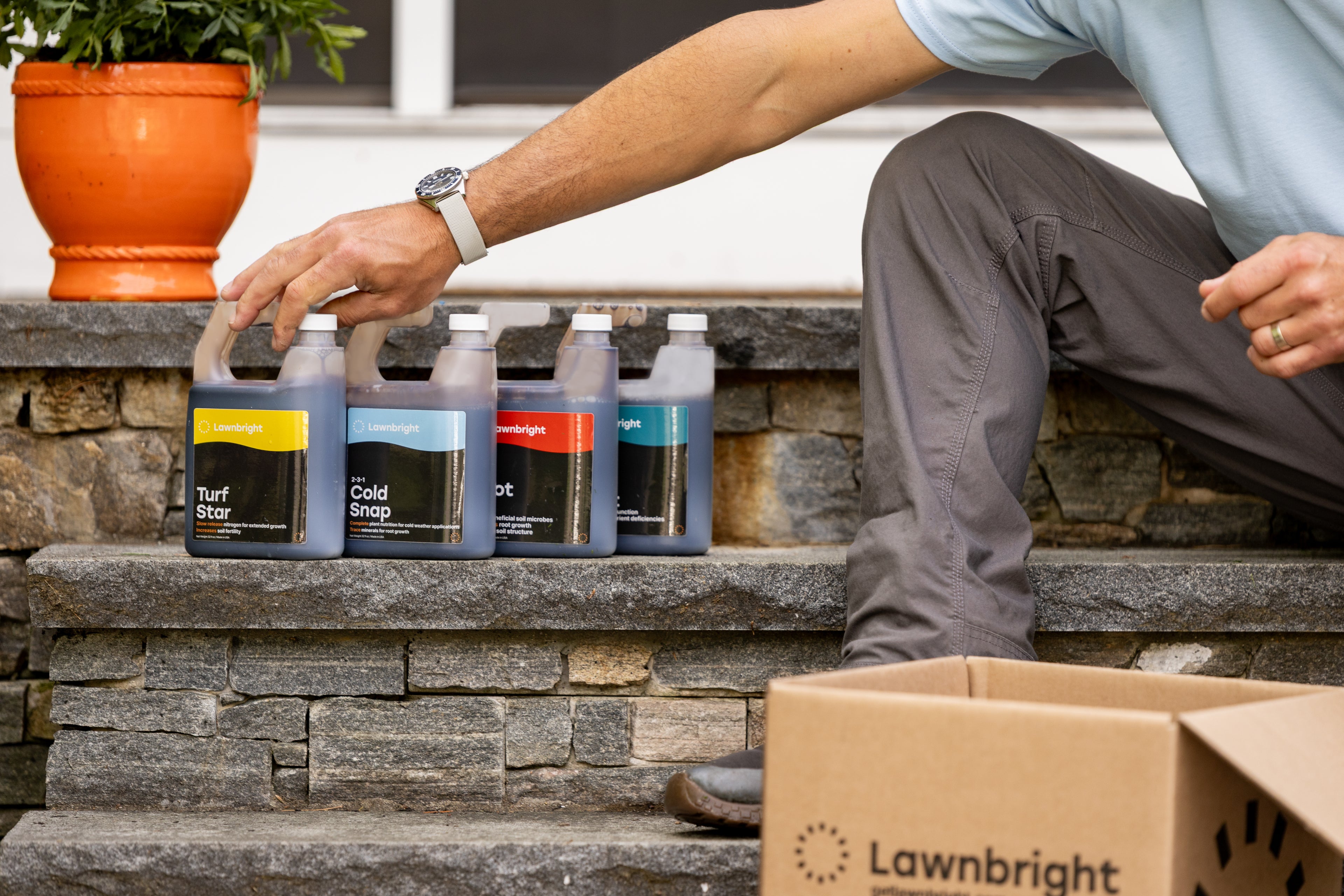 Person arranging bottles of Lawnbright products on stone steps with a cardboard box labeled Lawnbright.