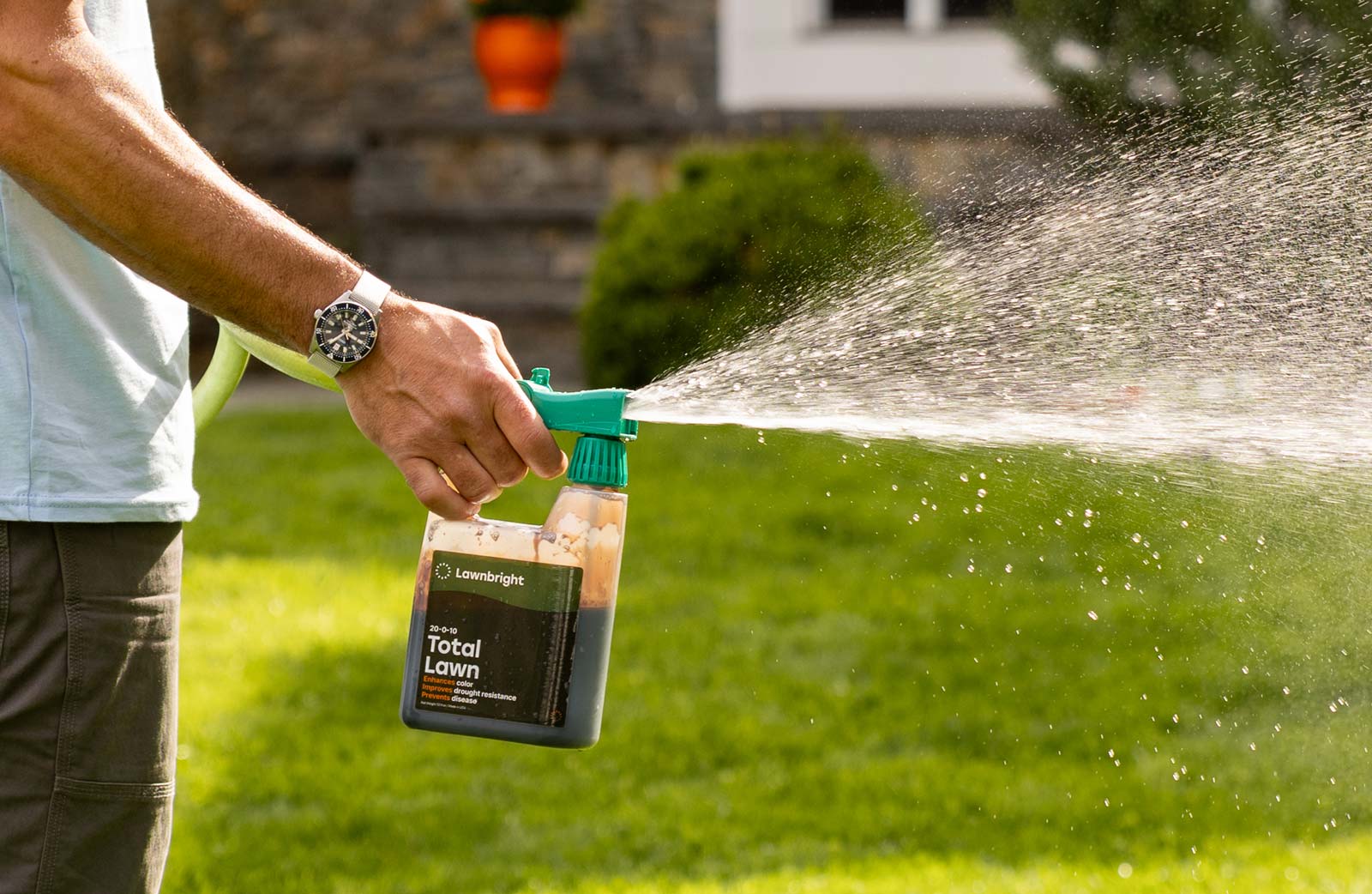 Person spraying a lawn care product via garden hose, labeled Lawnbright Total Lawn.
